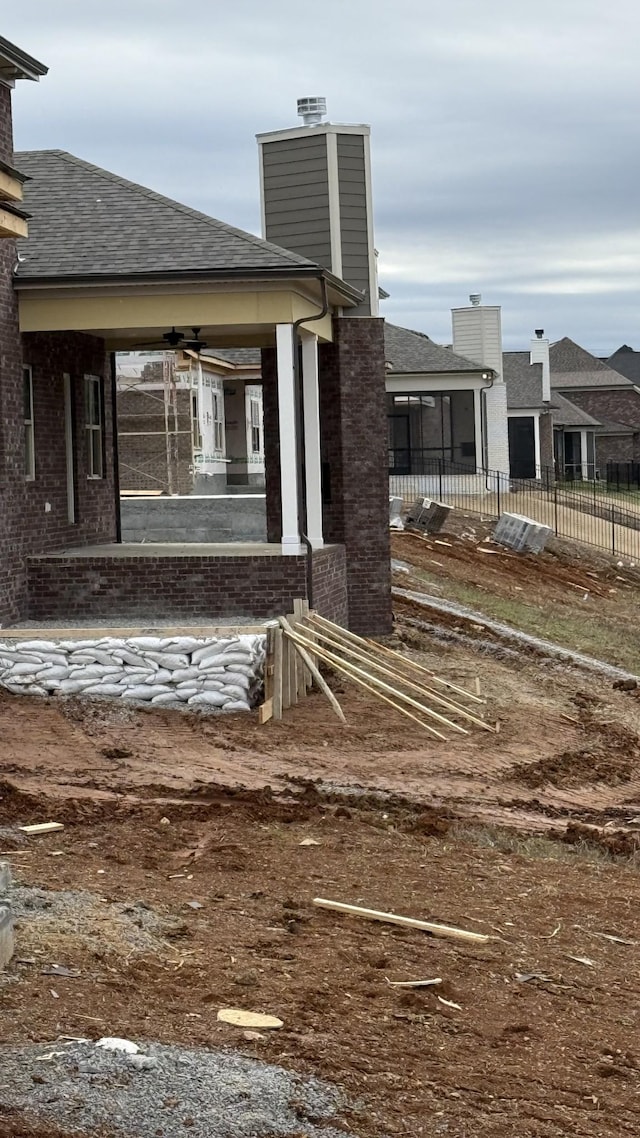 view of side of property with roof with shingles, brick siding, a chimney, a sunroom, and fence