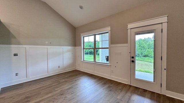 doorway featuring dark wood-style floors, lofted ceiling, wainscoting, and a decorative wall