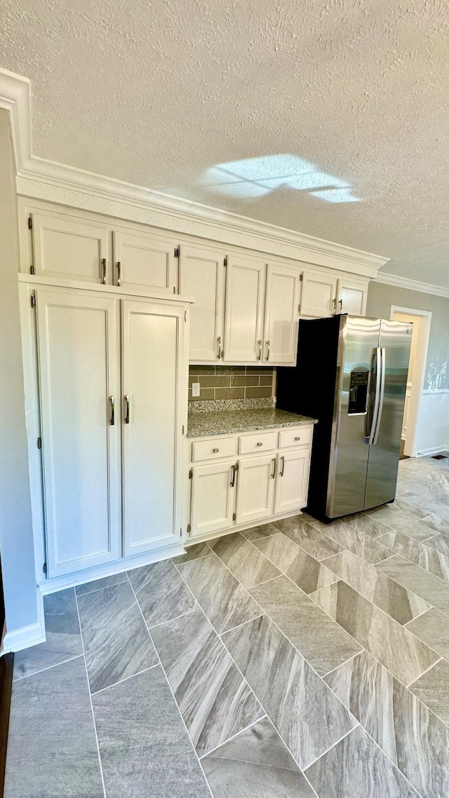 kitchen with a textured ceiling, white cabinetry, ornamental molding, stainless steel refrigerator with ice dispenser, and backsplash