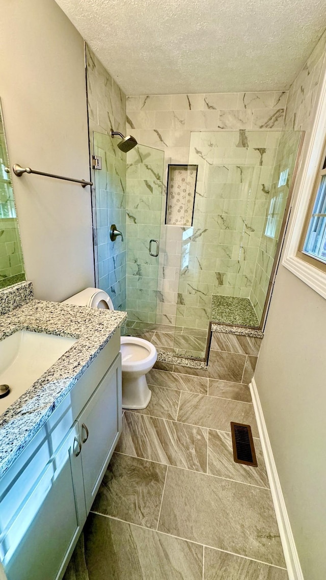 full bath with visible vents, a shower stall, a textured ceiling, vanity, and baseboards