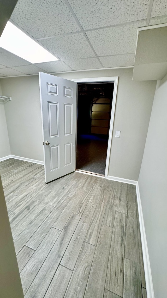 interior space with baseboards, a drop ceiling, and wood finished floors