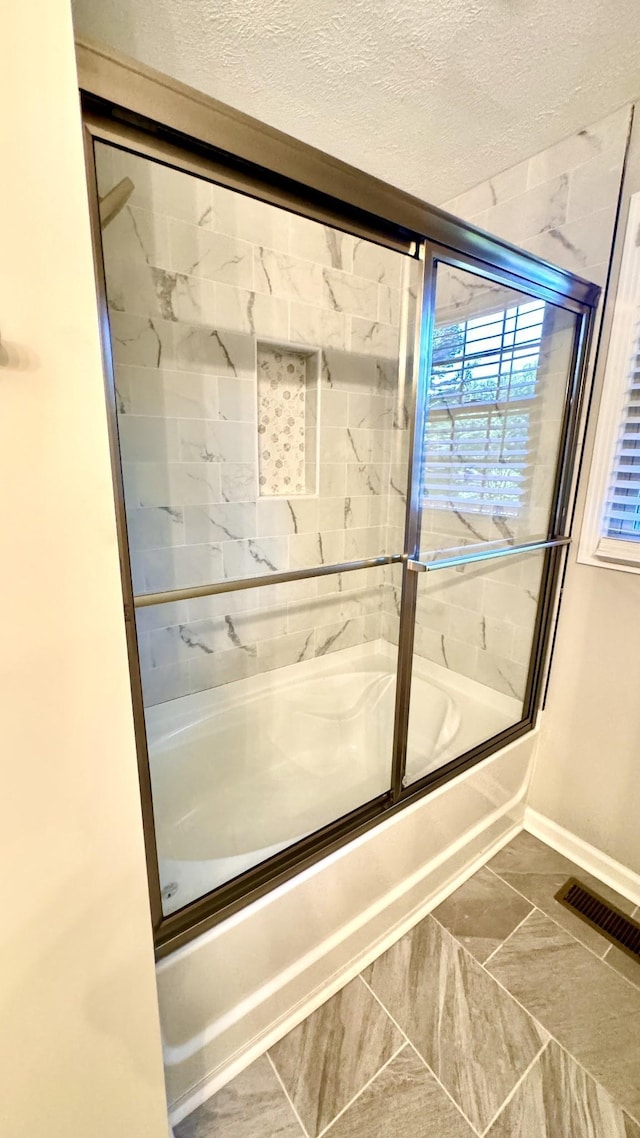 full bathroom featuring baseboards, visible vents, a textured ceiling, and combined bath / shower with glass door