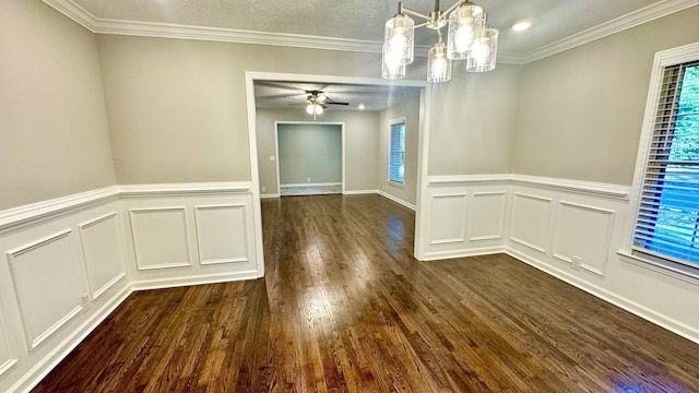 unfurnished dining area featuring ceiling fan with notable chandelier, dark wood-type flooring, a decorative wall, and crown molding