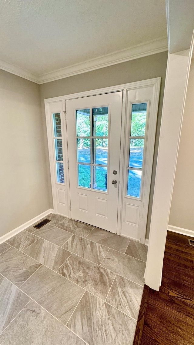 entryway with ornamental molding, visible vents, and baseboards