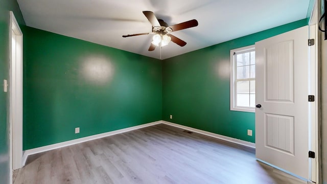 spare room featuring a ceiling fan, visible vents, baseboards, and wood finished floors