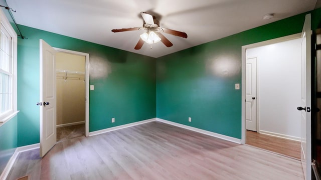 unfurnished bedroom with a closet, a spacious closet, a ceiling fan, wood finished floors, and baseboards