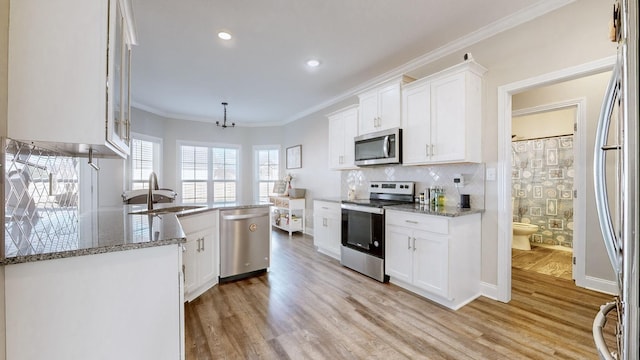 kitchen with stone counters, stainless steel appliances, white cabinetry, light wood finished floors, and crown molding