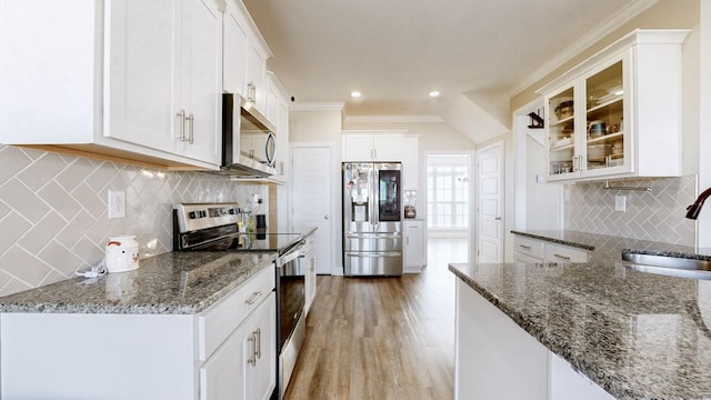 kitchen with appliances with stainless steel finishes, light wood-style floors, ornamental molding, a sink, and dark stone countertops