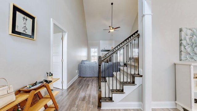 stairs featuring high vaulted ceiling, wood finished floors, a ceiling fan, and baseboards