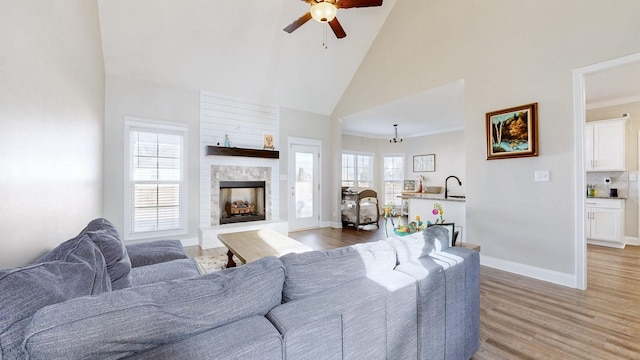 living area featuring a fireplace with raised hearth, high vaulted ceiling, plenty of natural light, and light wood-style flooring