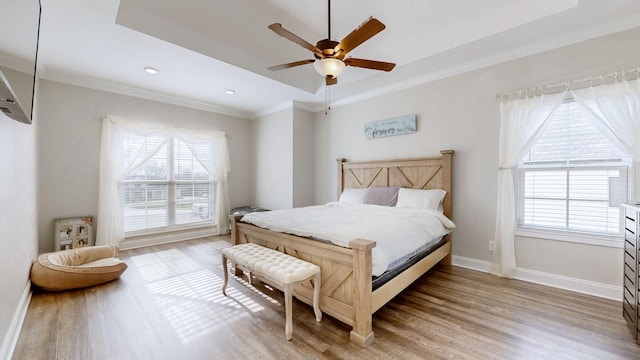 bedroom featuring baseboards, a raised ceiling, a ceiling fan, ornamental molding, and light wood-style floors