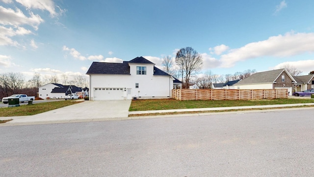 view of side of property featuring a garage, concrete driveway, a residential view, fence, and a yard