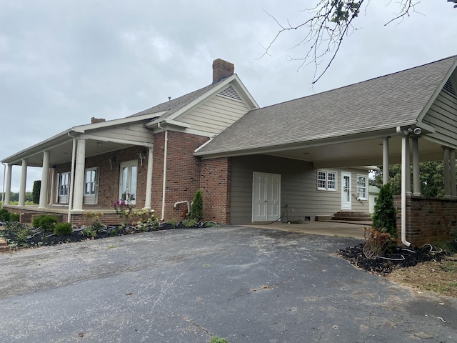 view of front facade with a shingled roof, a chimney, aphalt driveway, an attached carport, and brick siding