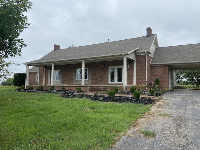 view of front of house featuring french doors, brick siding, a chimney, a front yard, and driveway