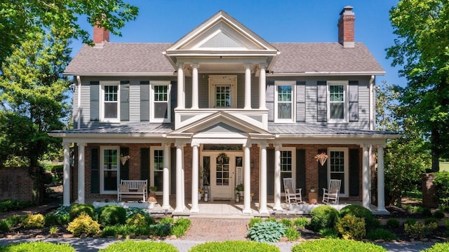 neoclassical / greek revival house featuring a chimney, a porch, and brick siding