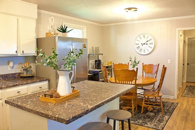 kitchen featuring light wood finished floors, a breakfast bar, freestanding refrigerator, and white cabinets