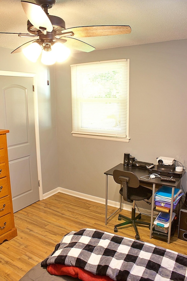 office area featuring a textured ceiling, baseboards, a ceiling fan, and light wood-style floors