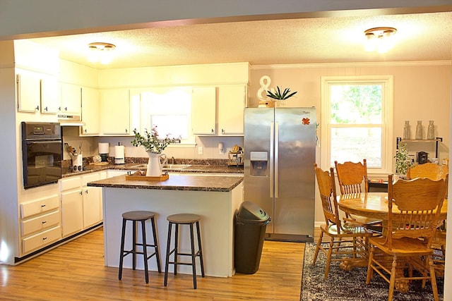 kitchen with dark countertops, black appliances, ornamental molding, and light wood-style floors