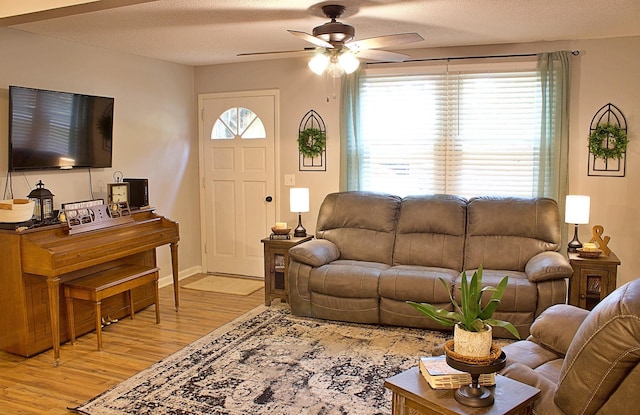 living room featuring baseboards, ceiling fan, light wood-style flooring, and a textured ceiling