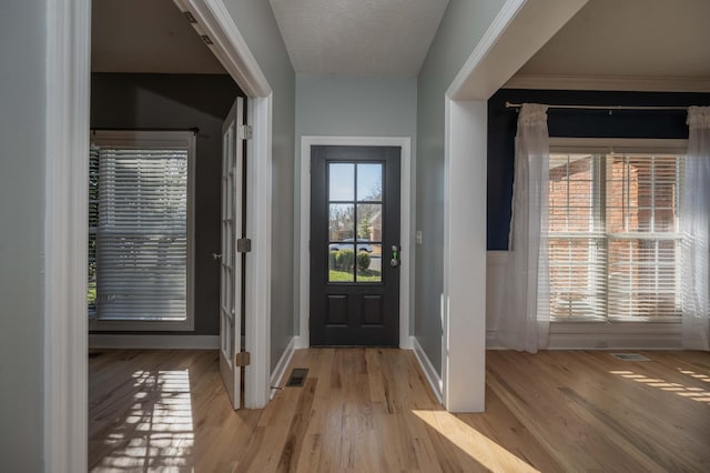 foyer entrance with light wood-type flooring, visible vents, a textured ceiling, and baseboards