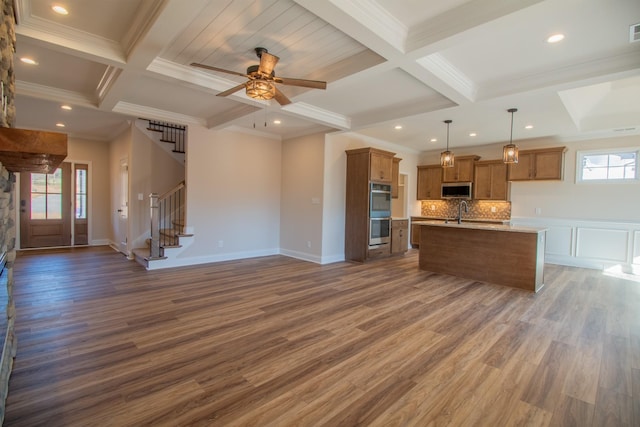 kitchen with stainless steel appliances, coffered ceiling, open floor plan, beam ceiling, and brown cabinetry