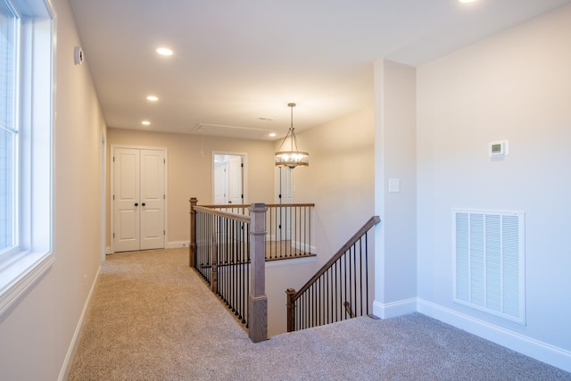 hall featuring an upstairs landing, carpet flooring, visible vents, and attic access