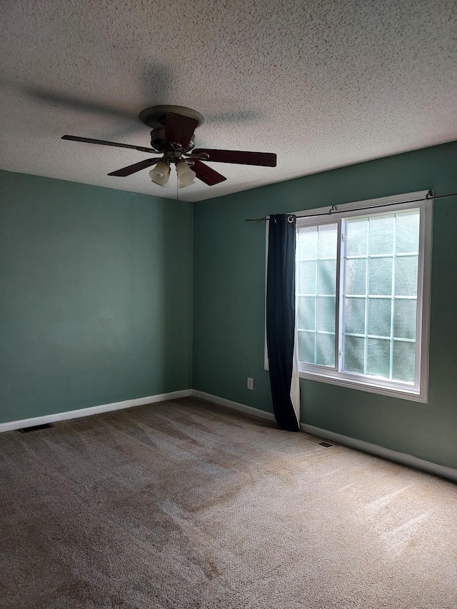 empty room with a textured ceiling, carpet, a ceiling fan, and baseboards