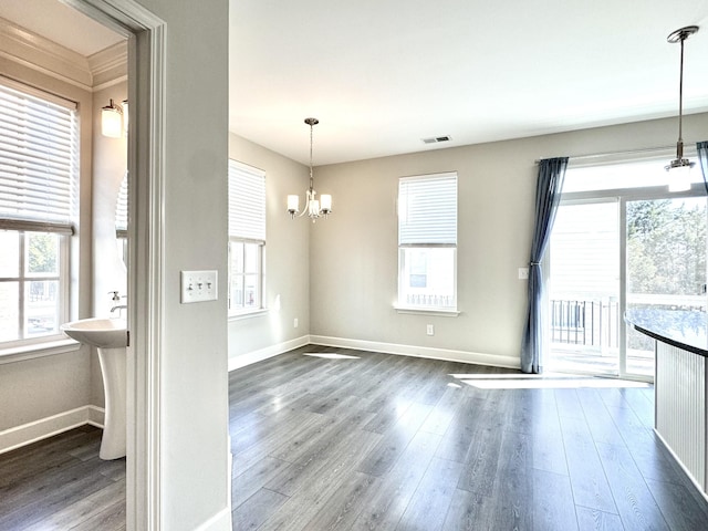 unfurnished dining area featuring a chandelier, visible vents, baseboards, and wood finished floors