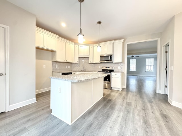 kitchen with hanging light fixtures, appliances with stainless steel finishes, light wood-style floors, and tasteful backsplash