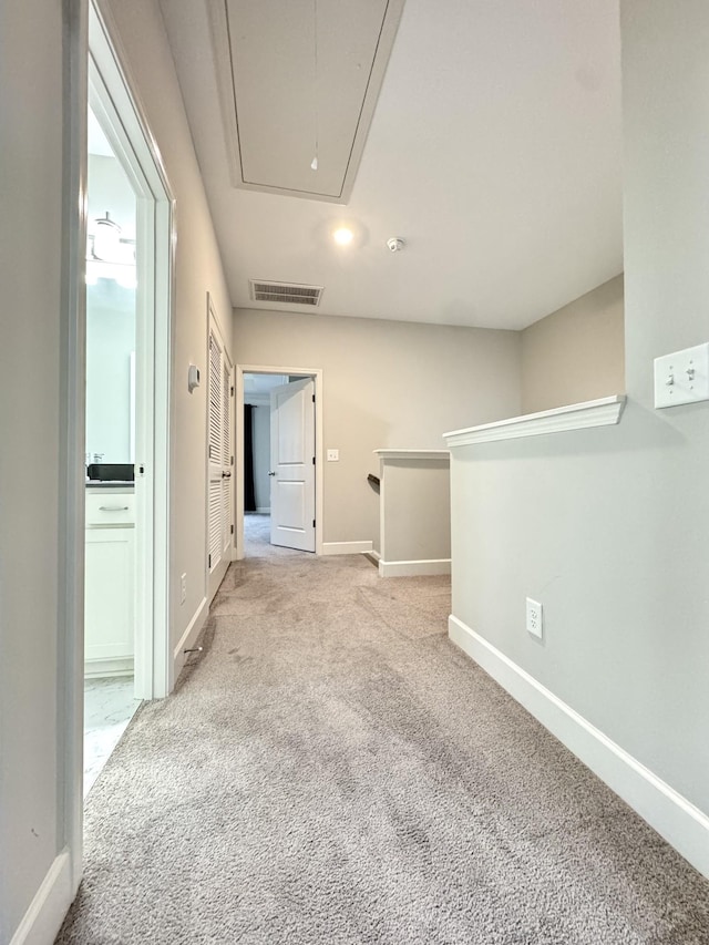 corridor with light carpet, attic access, visible vents, and baseboards