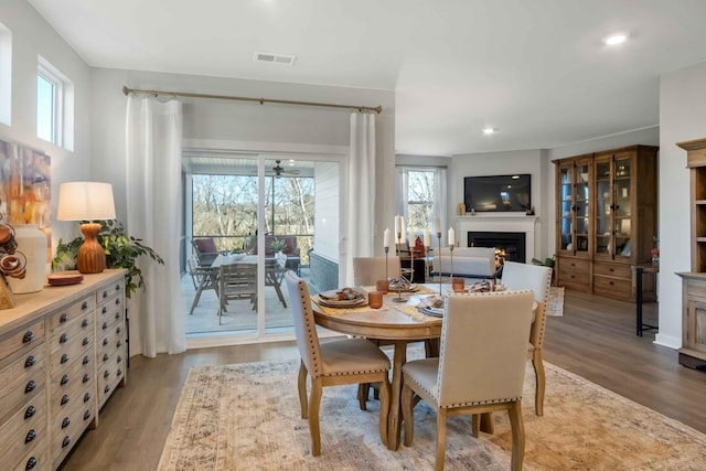 dining area with a warm lit fireplace, wood finished floors, visible vents, and a healthy amount of sunlight