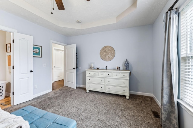 bedroom featuring dark colored carpet, a tray ceiling, visible vents, and baseboards