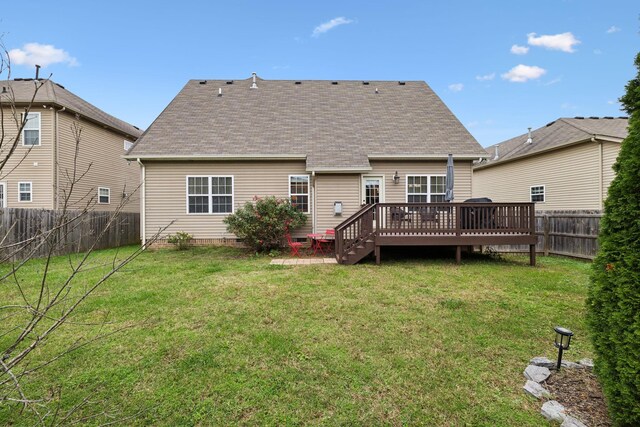 rear view of house with a fenced backyard, a shingled roof, a deck, and a lawn