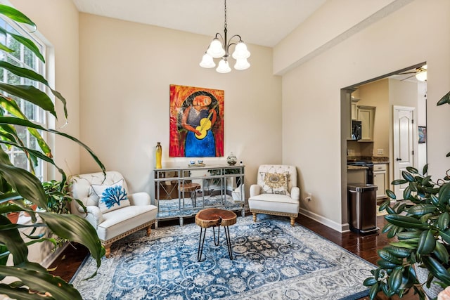 living area with baseboards, dark wood-type flooring, and ceiling fan with notable chandelier