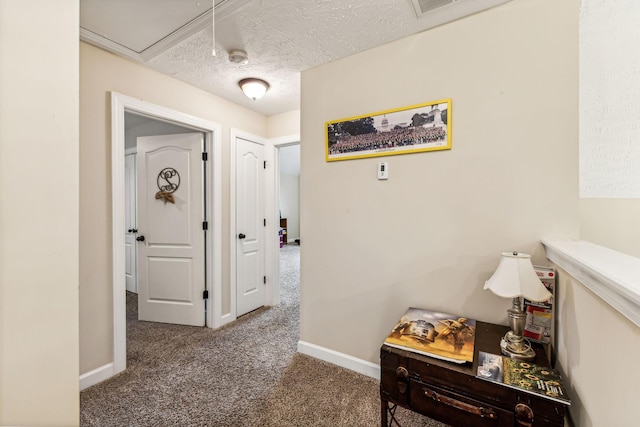 hall featuring a textured ceiling, carpet, attic access, and baseboards