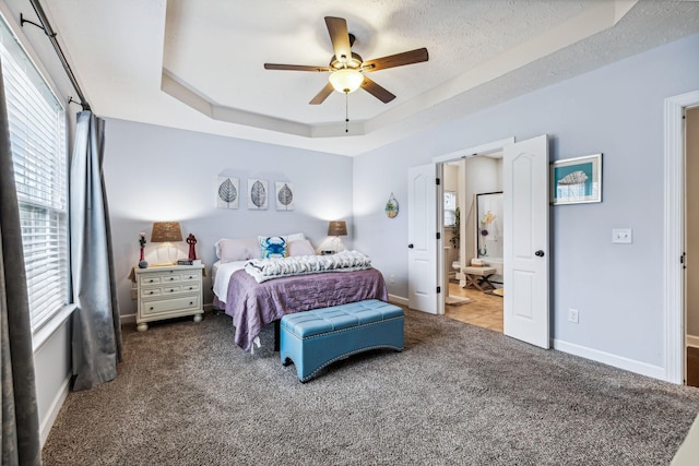 bedroom featuring baseboards, ensuite bathroom, a tray ceiling, a textured ceiling, and carpet flooring