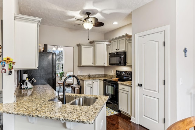 kitchen featuring a peninsula, light stone countertops, a textured ceiling, black appliances, and a sink