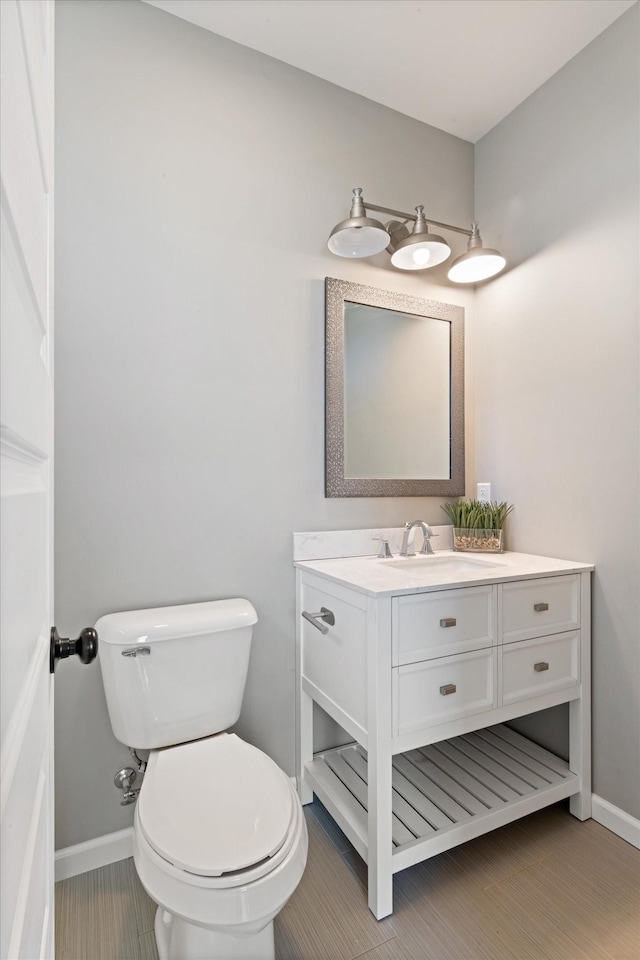 half bathroom with toilet, baseboards, and vanity