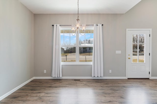 unfurnished dining area with a healthy amount of sunlight, a notable chandelier, baseboards, and wood finished floors