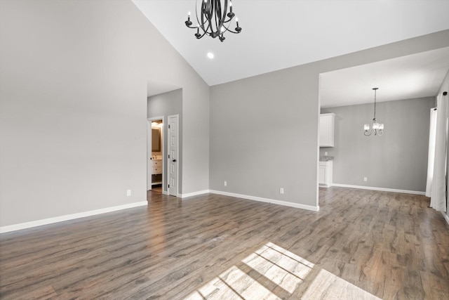 unfurnished living room with a chandelier, high vaulted ceiling, wood finished floors, and baseboards