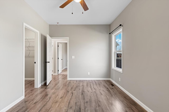 unfurnished bedroom featuring a closet, a spacious closet, a ceiling fan, wood finished floors, and baseboards