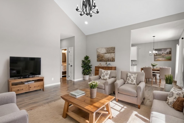 living room featuring a chandelier, high vaulted ceiling, light wood-type flooring, and baseboards