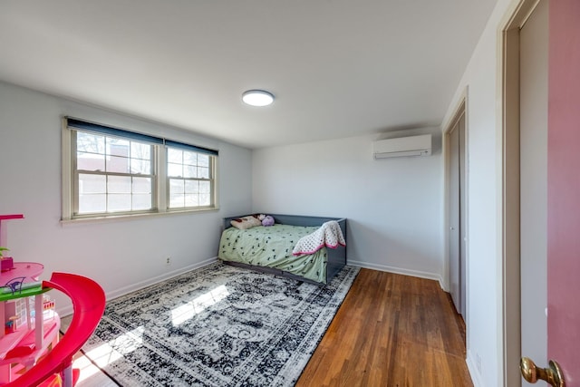 bedroom with baseboards, an AC wall unit, and wood finished floors