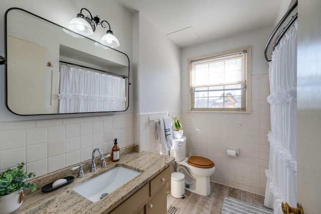 full bath with wainscoting, toilet, wood finished floors, vanity, and tile walls