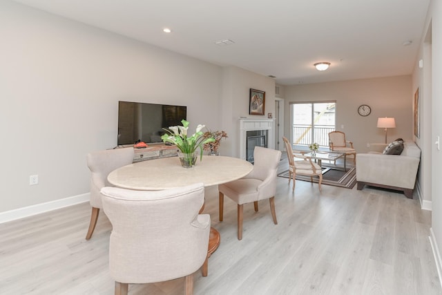 dining space with recessed lighting, baseboards, a glass covered fireplace, and light wood finished floors