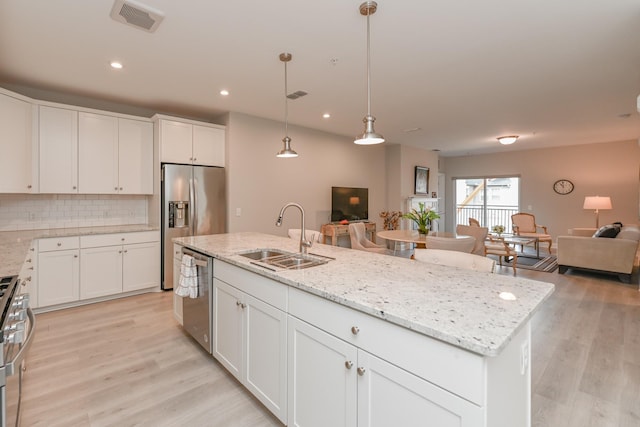 kitchen with light wood finished floors, a sink, appliances with stainless steel finishes, open floor plan, and backsplash