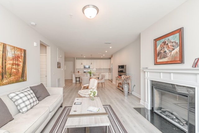 living room featuring visible vents, a fireplace with flush hearth, and light wood finished floors