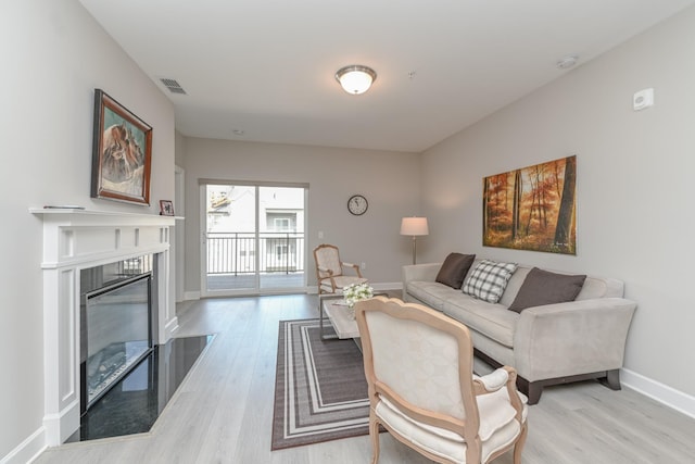 living room featuring light wood-style flooring, a fireplace with flush hearth, baseboards, and visible vents