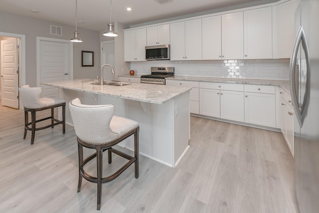 kitchen with visible vents, light wood finished floors, a sink, decorative backsplash, and stainless steel appliances