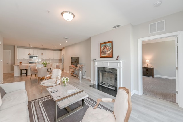 living room featuring visible vents, baseboards, light wood-type flooring, and a fireplace with flush hearth